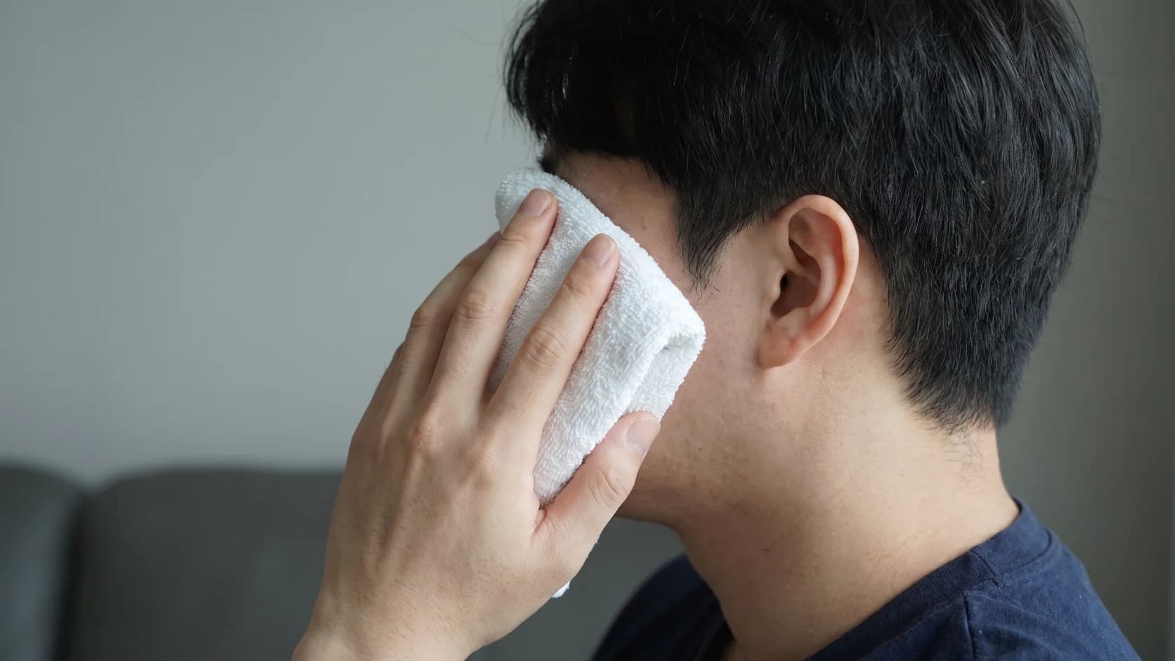 눈이 보이지 않는 옆뒤 구도에서 천으로 감싼 냉찜질을 바깥 관자 부위에 가볍게 대는 모습