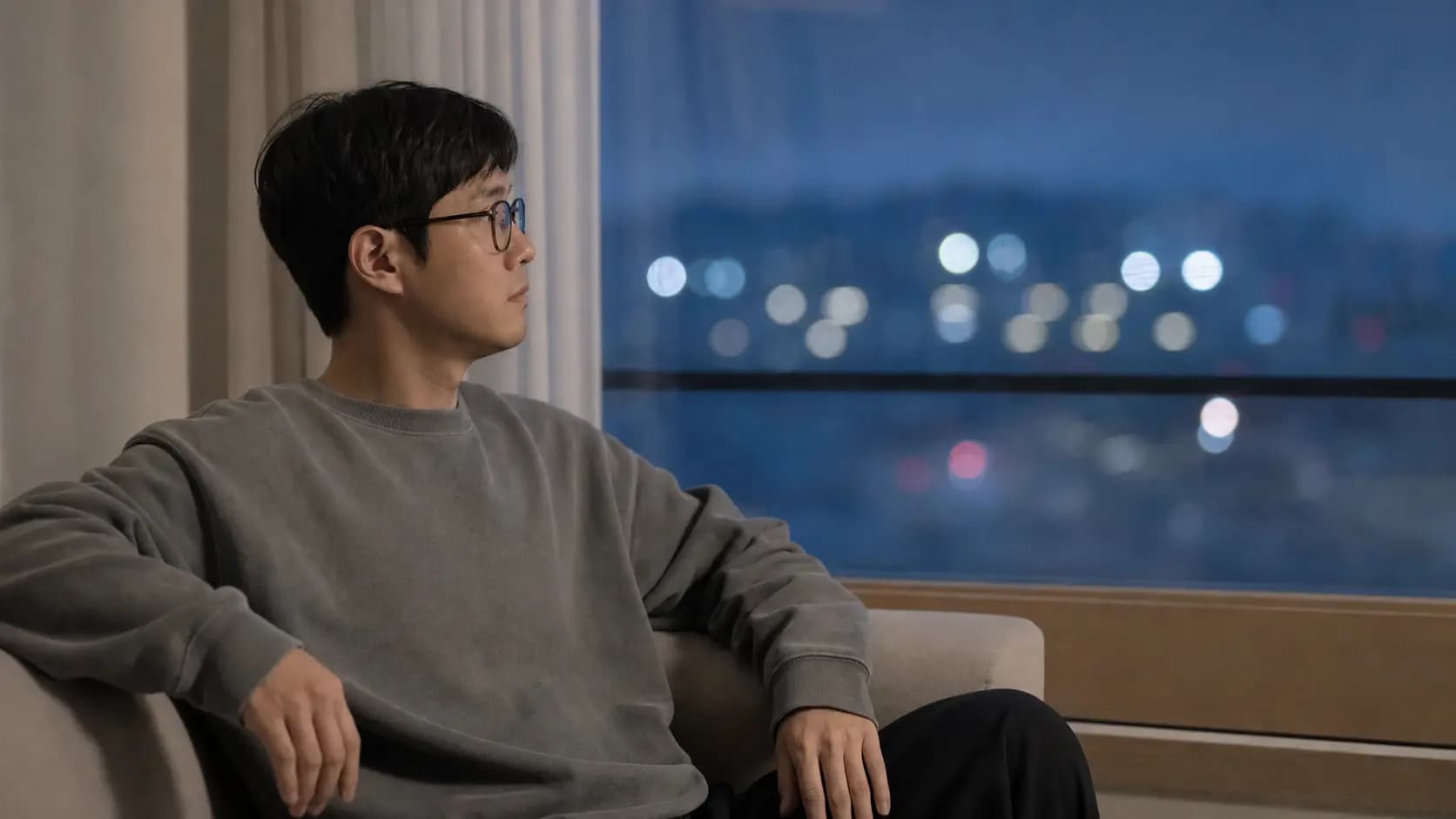 안경을 쓰고 저녁 창밖의 흐린 불빛을 바라보는 성인